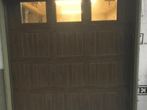 Dark brown carriage-style garage door with raised panels and three glass windows