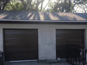 Two black roll-up garage doors on brick garage with horizontal slat panels