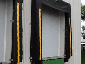 White commercial garage door with black trim and yellow safety edge guards on concrete structure